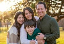 A mom, a dad and their two children huddle together for a sunny photo outdoors.