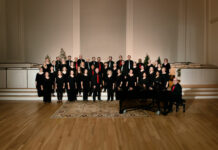 A group of choral members from the Choral Arts Society of Frederick stands indoors in black uniforms on wood floors. The multigenerational group is celebrating its 80th season.