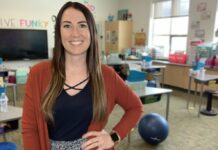 Casey Jeffers, a young woman smiles with her hand on her hip. She's in a classroom.