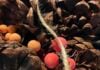 Red and orange beads nestled in a pile of pinecones and draped with beige twine