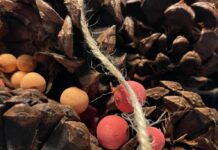 Red and orange beads nestled in a pile of pinecones and draped with beige twine