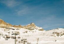 Bunny Slopes and Green Circles: The 5 Best Beginner Ski Resorts Nearby People skiing on a snowy expanse underneath a chair lift. The sky above is clear and blue.