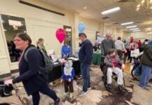 Photo of a child holding a balloon in a large conference room with tables set up and people milling around.