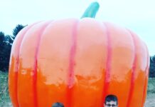Children with pumpkins sit in front of a giant pumpkin statue