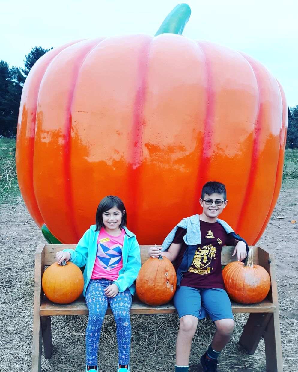 Children with pumpkins sit in front of a giant pumpkin statue