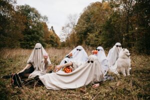 People dressed as ghosts pose on a field with a dog