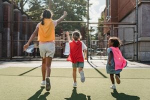 Three kids wearing capes run away from the camera