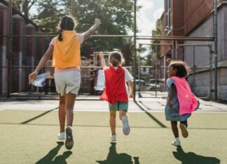 Three kids wearing capes run away from the camera