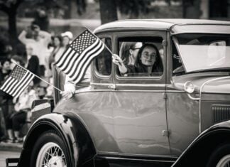 A girl holds an American flag out a car window at a Fourth of July parade