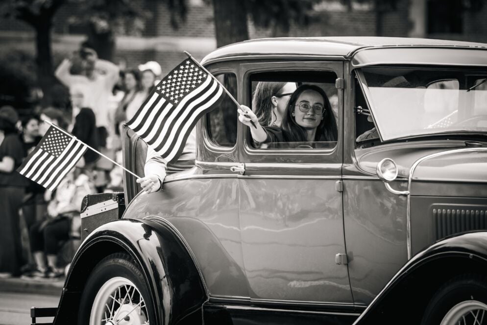 A girl holds an American flag out a car window at a Fourth of July parade
