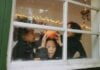 Three kids play by a window looking out on Halloween. One is holding a pumpkin and making a silly face.